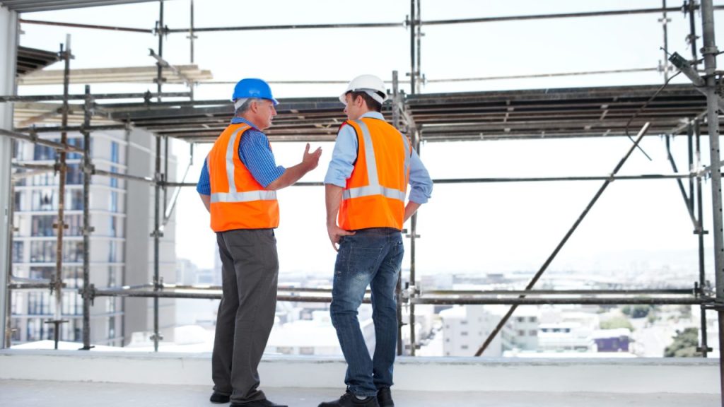 Two construction supervisors talking on a scaffolded building deck