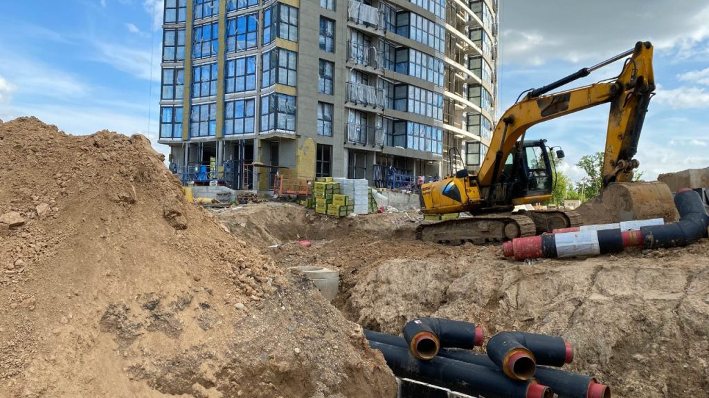 Excavator trenching for utilities beside a multi-story building