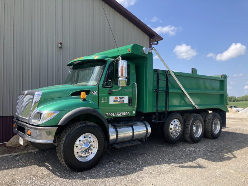 Green NWI Builders dump truck parked beside a pole barn