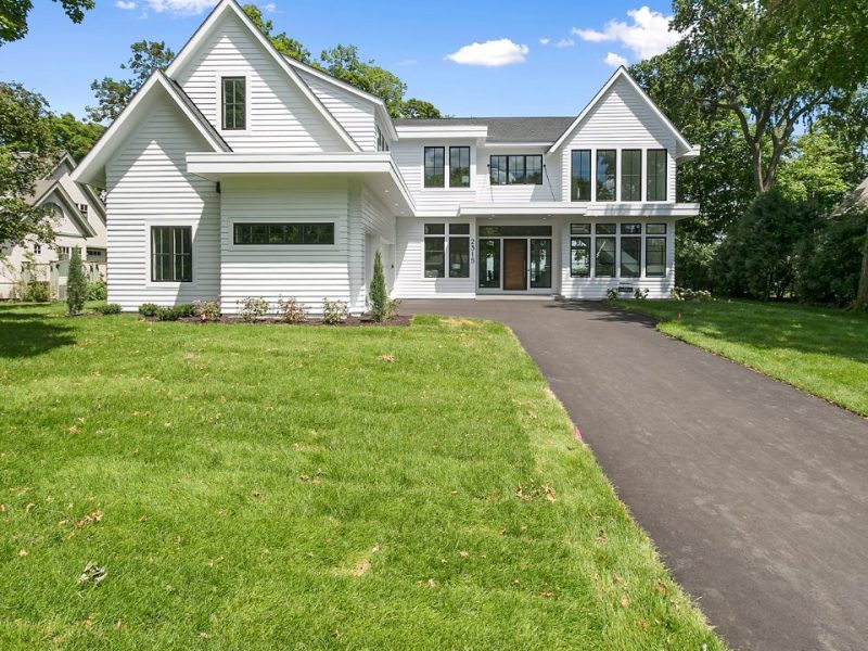 Large white farmhouse-style home with a landscaped lawn and driveway