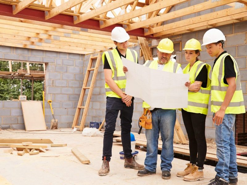 Construction crew reviewing plans inside a partially framed building