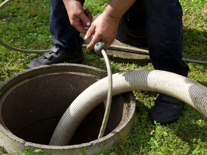 Technician feeding a suction hose into a septic tank access riser